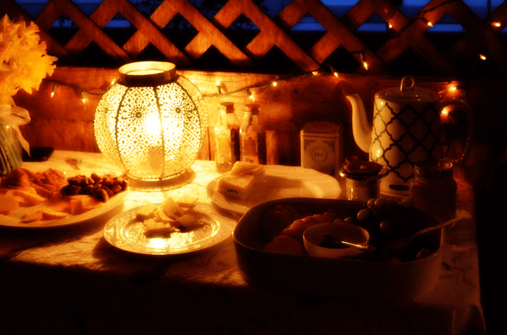 The food table is dimly lit by twinkling lights and a lamp next to an elegant electric tea kettle
