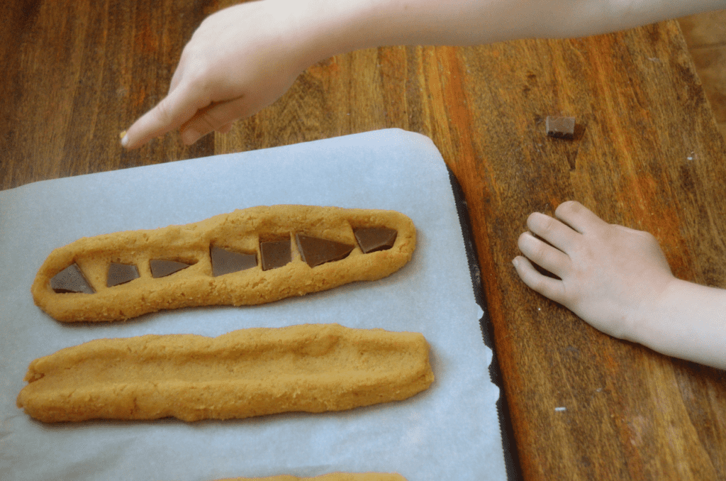 A little hand points at a cookie dough log with chocolate in place of jam in middle indent