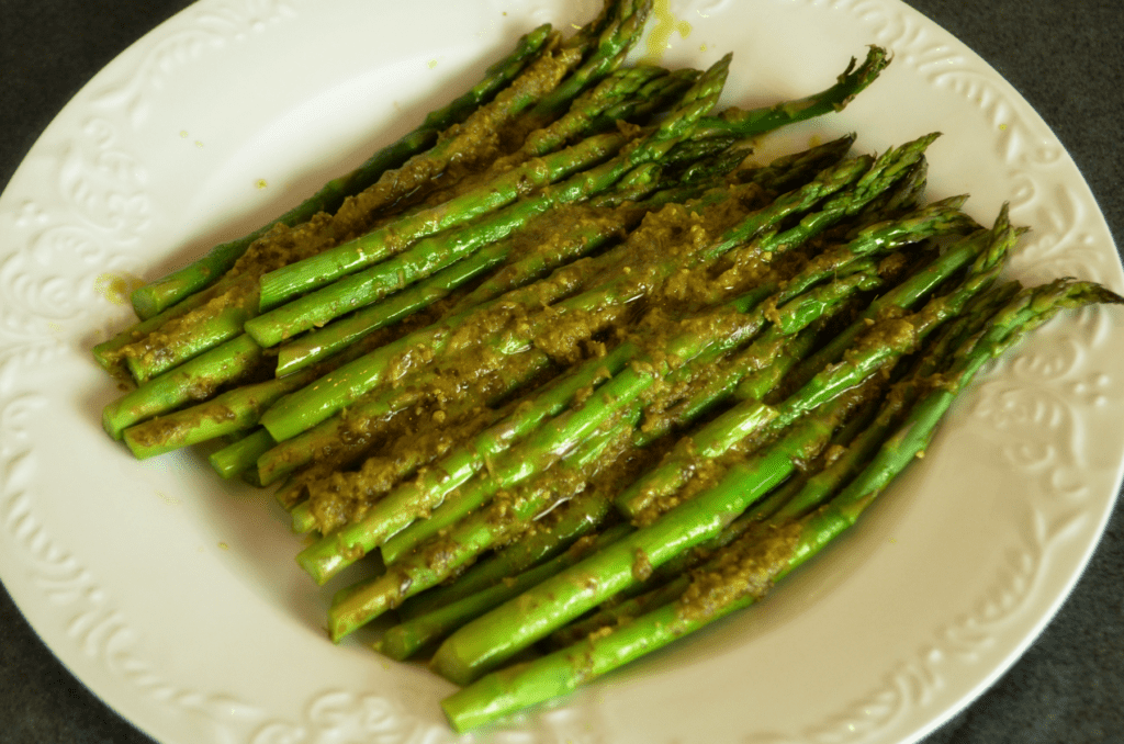 Cooked asparagus with basil pesto lay on bright white serving platter