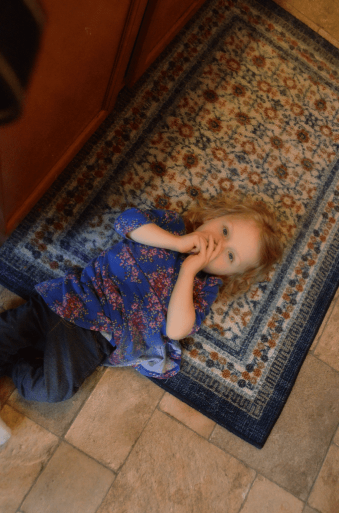 child laying on a rug on the floor and sucking thumb