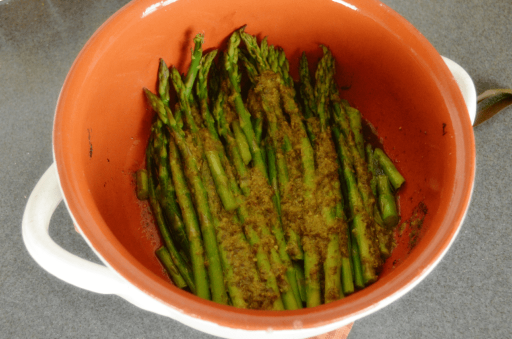 cooked asparagus coated with basil pesto in ceramic round dish