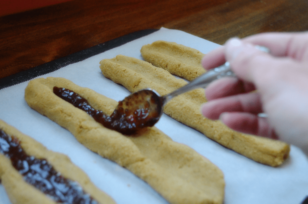 hand places jam inside the indent of a cookie dough log in preparation to bake