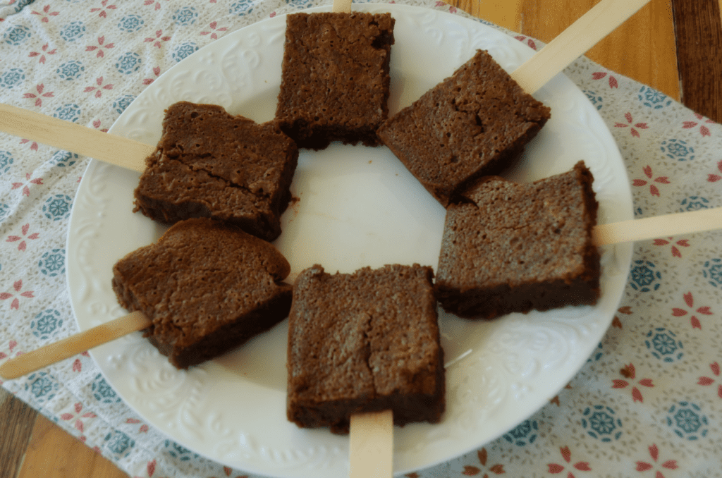 Six brownies on a white plate make a sunshine shape with the brownie towards the center and sticks stretching out from the plate.