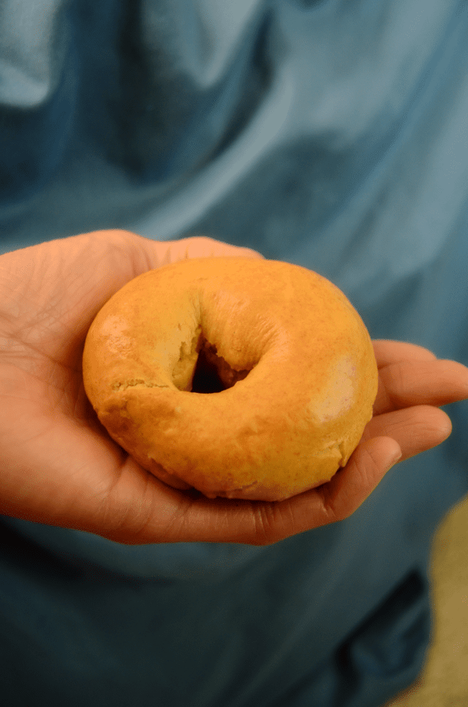 A hand holds a single golden bagel with a blue background