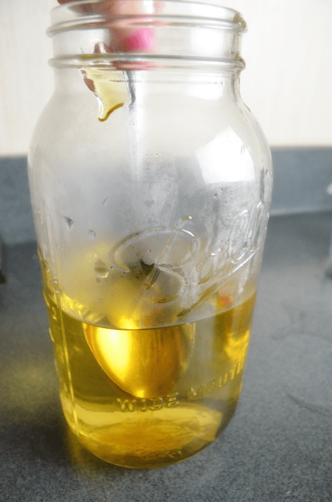 A spoon stirs honey into tea in a large Ball canning jar.