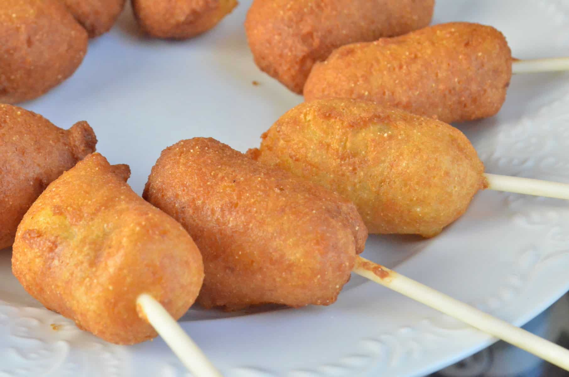Freshly fried corndogs lay around a plate