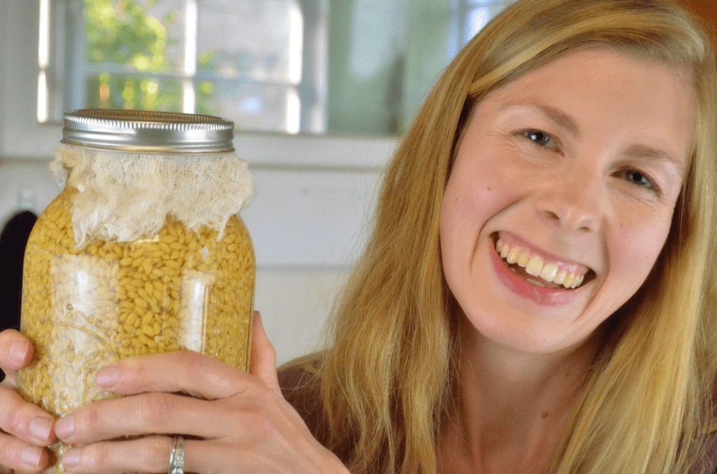 lady smiles while she holds a jar of grain soaking in water