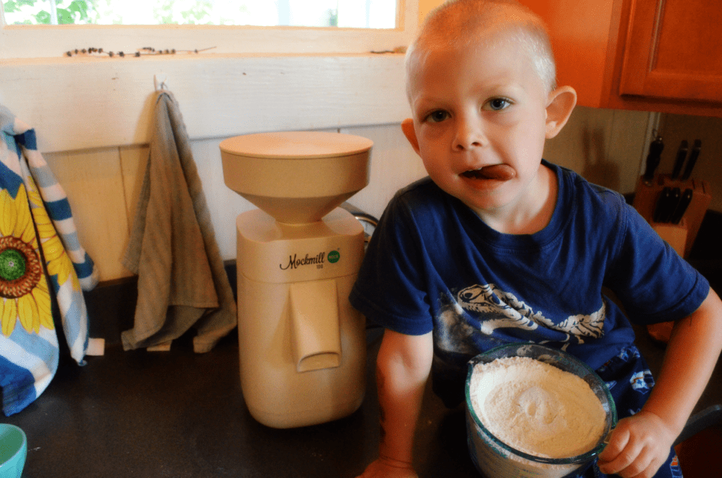 Little boy sits on a countertop next to a mockmill 100 flour mill 