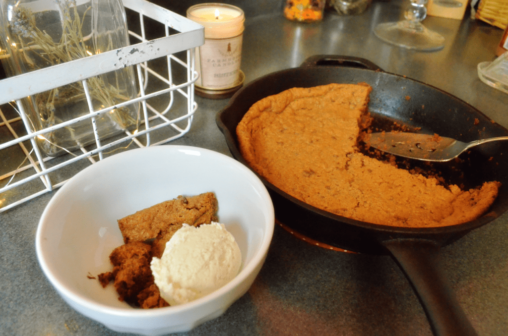 skillet cookie sits on a counter next to a white bowl filled with cookie and creamy vanilla ice cream