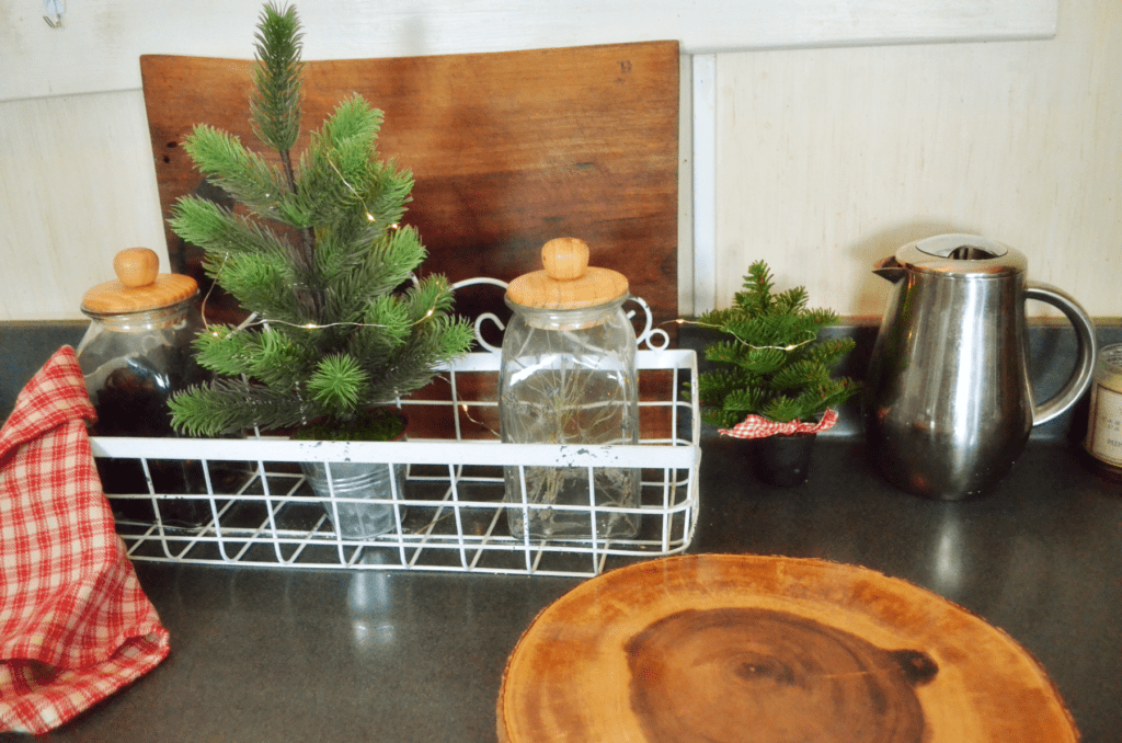 Golden wood cuttings boards are displayed on a kitchen counter among shine glass containers and festive winter tree decorations.