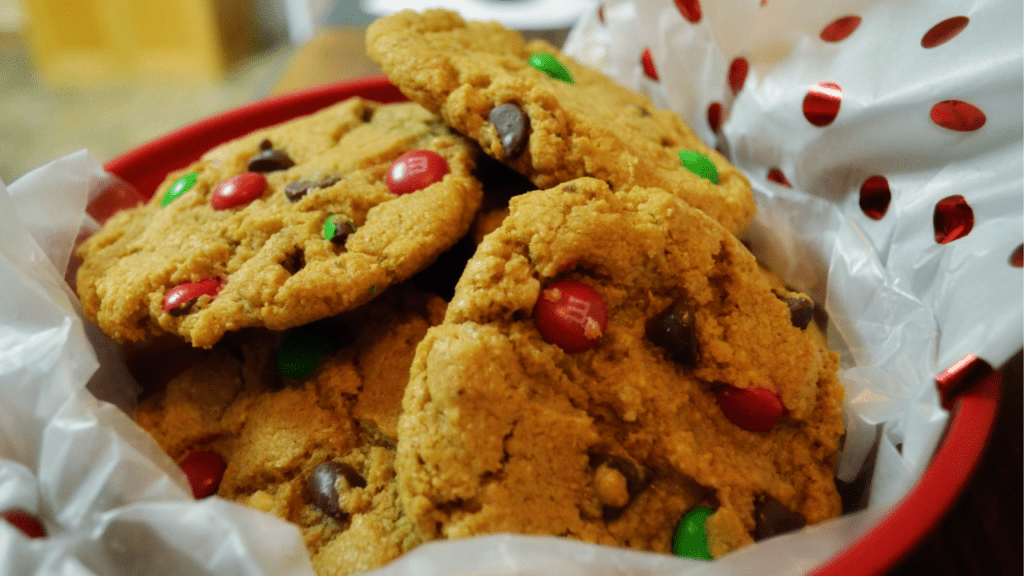 Red and Green dotted Chocolate Chip Cookies overflow from a festive tissue lined cookie tin.