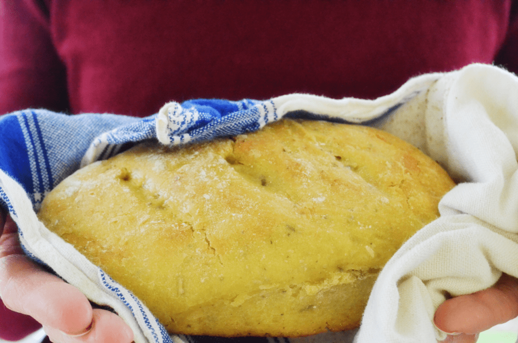 hands hold a white and blue tea towel with fresh bright sourdough garlic bread inside.