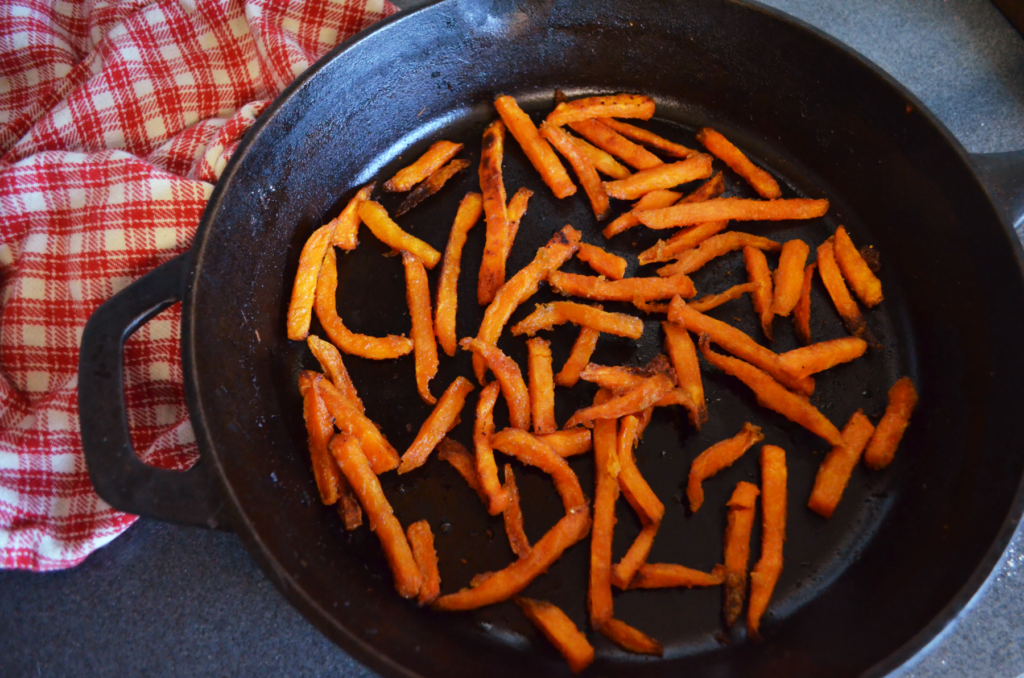 Look straight down over a large cast iron pan. The darkness is contrasted by the bright orange fries. Edges bubbly and crispy, they are hot and ready to be served.