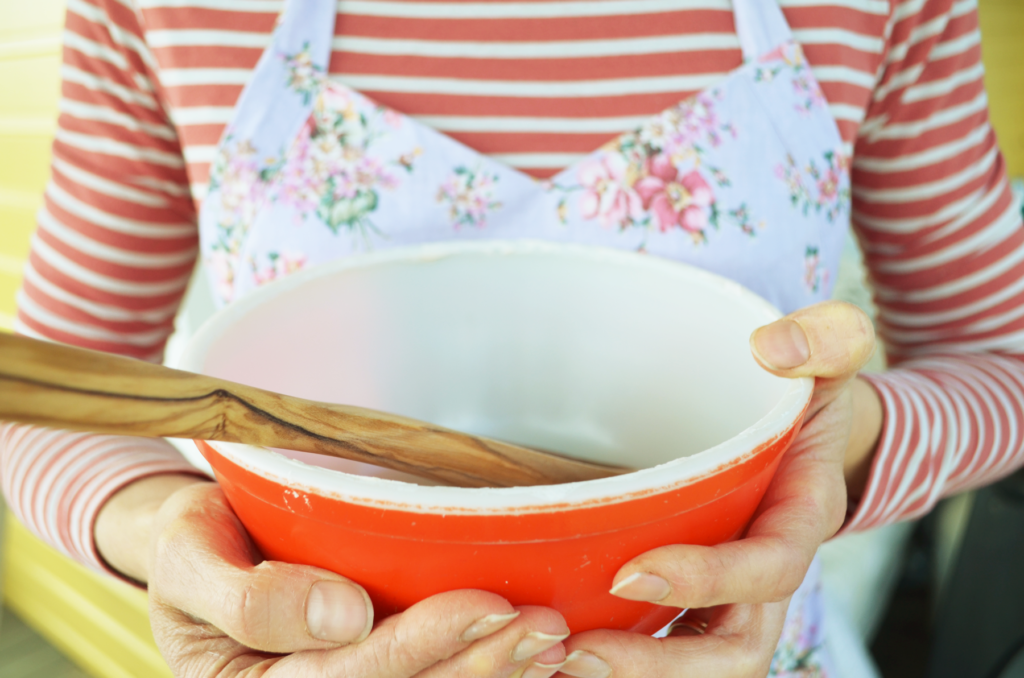 These hands learned how to bake with einkorn flour by time and patience. They hold a bright red bowl for mixing batters and dough. 