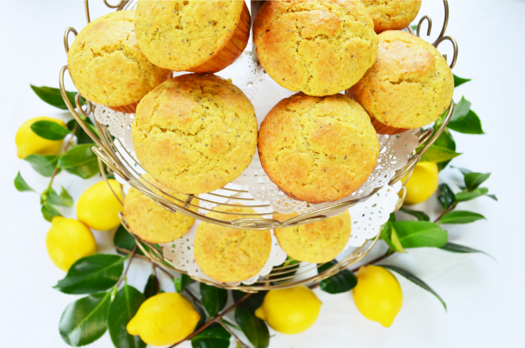 A beautiful Display tower shows beautiful results of the Sourdough Einkorn Lemon Poppy Seed Muffin recipe. Bright Lemons with lively green leaves sit underneath the display.