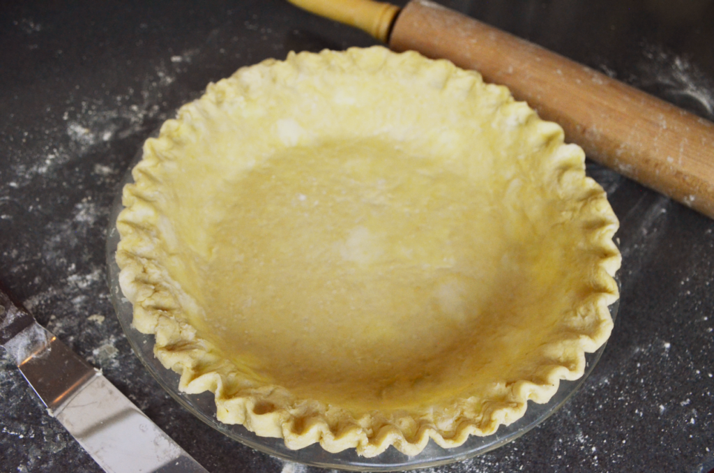 A flaky pie crust sits ready to be baked on a lightly floured countertop.