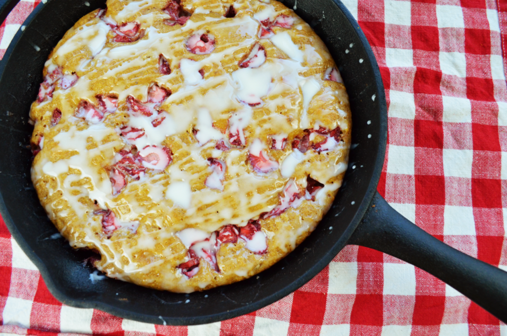 A cast iron with freshly bake strawberry scones sits on a festive red gingham tablecloth.