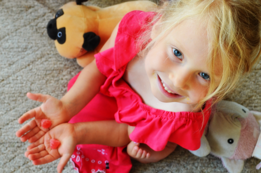 A young girl holds two vitamins and smiles at the camera. 