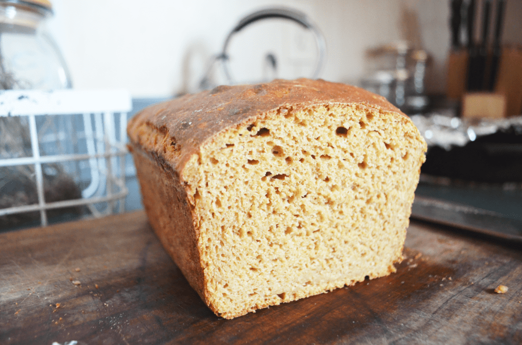 A Whole Grain Einkorn Flour Sandwich loaf sits atop a cutting board, the soft bread exposed from slicing. This is one of the best breads for acid reflux relief.