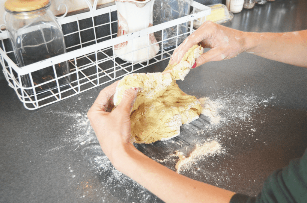 Hands fold dough on a dark counter, puffs of powdery einkorn flour spreading throughout the area