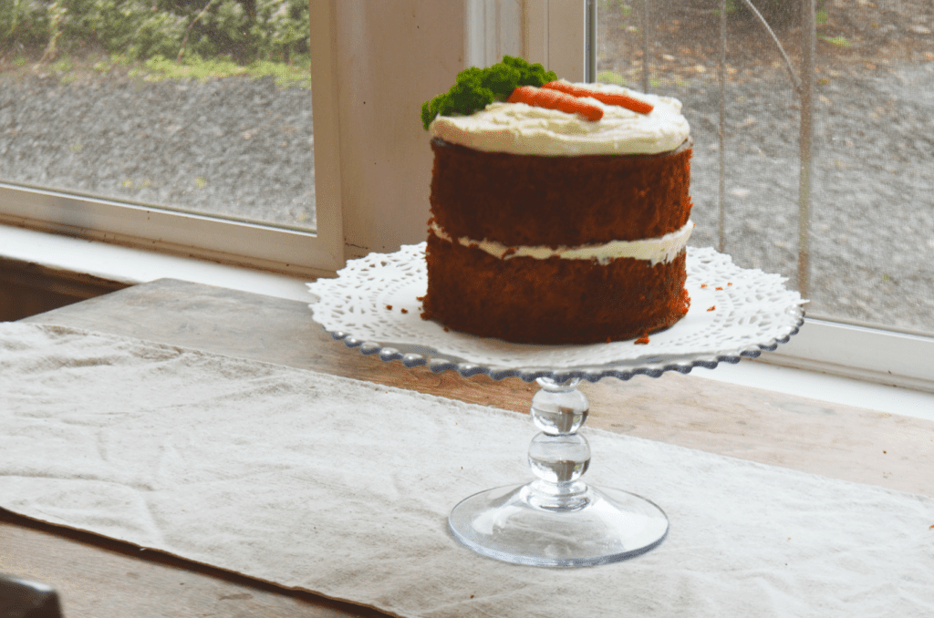The completed moist two layer carrot cake made with einkorn flour sits in front of the window light waiting to be cut.