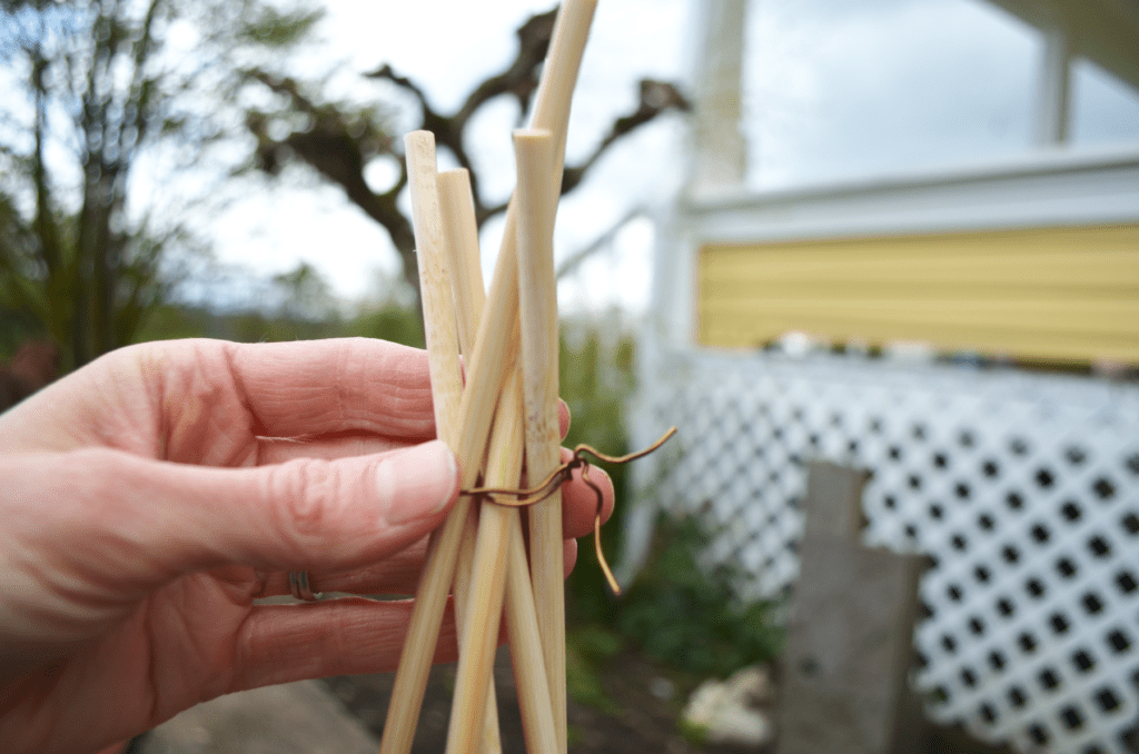 a hand tightens wire around the top of a wooden trellis for potted plants.