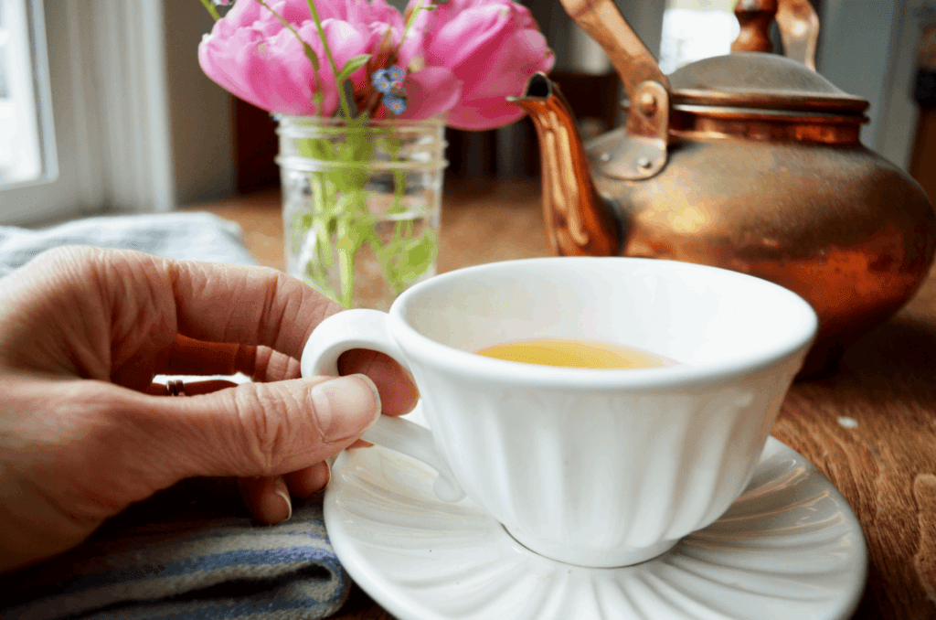 A hand holds a bright white ridged tea cup in the morning light. 
