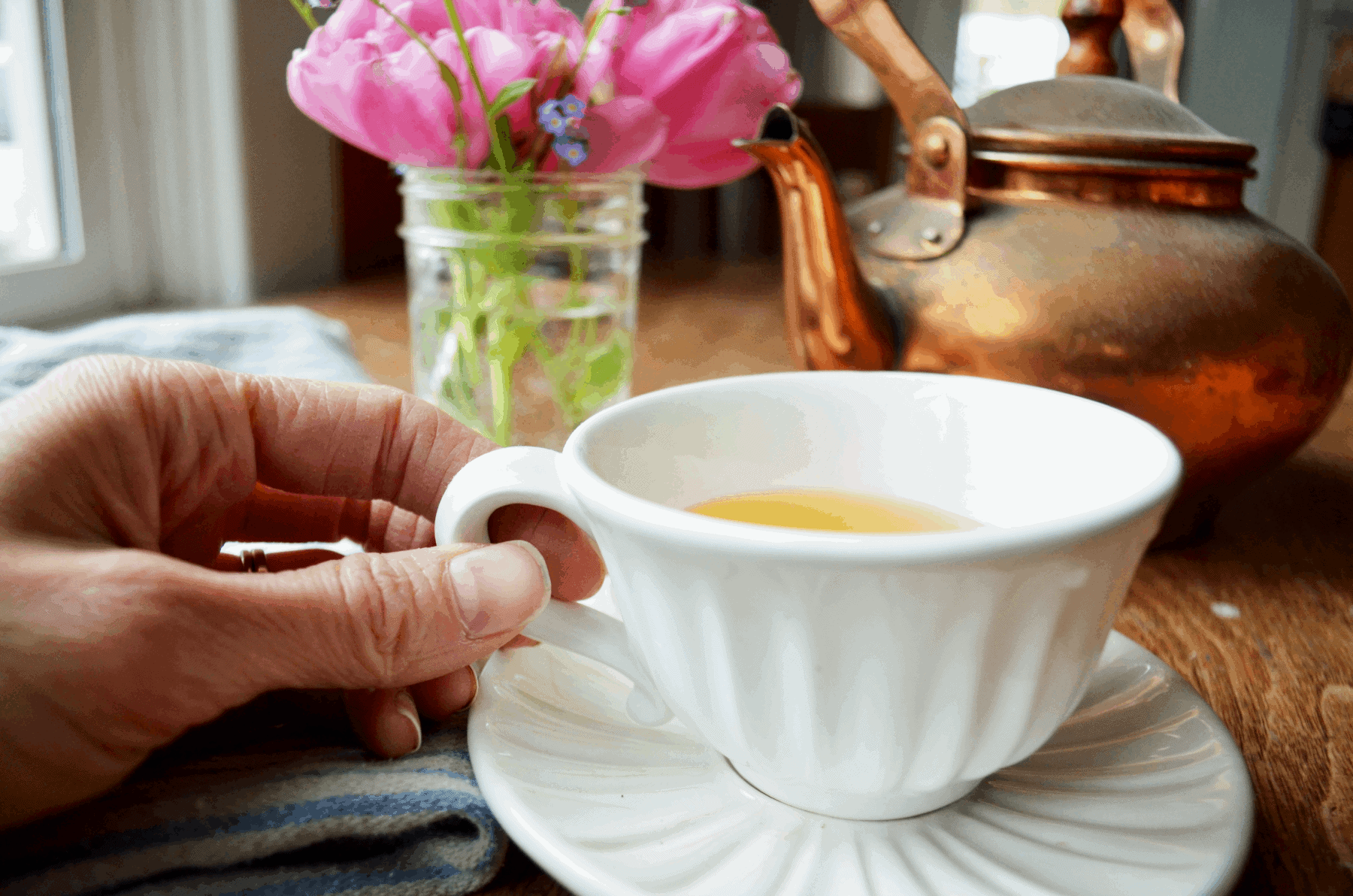 a hand holds the handle of a white tea cup filled with tea for women's hormones