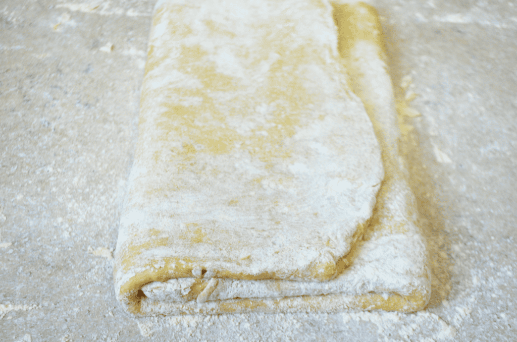 Flour dusted dough has been rolled flat and then folded like a letter to laminate for a croissant pastry.