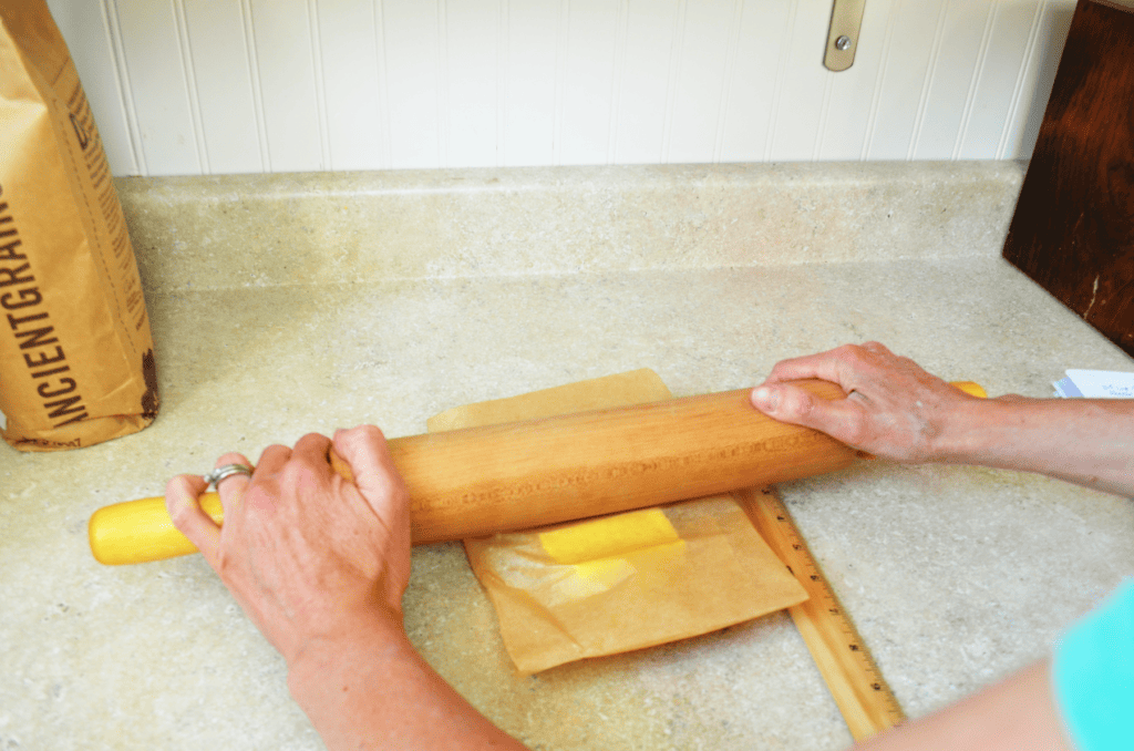 two arms push hard on cold butter in between parchment to mold it into the right shape for laminating dough