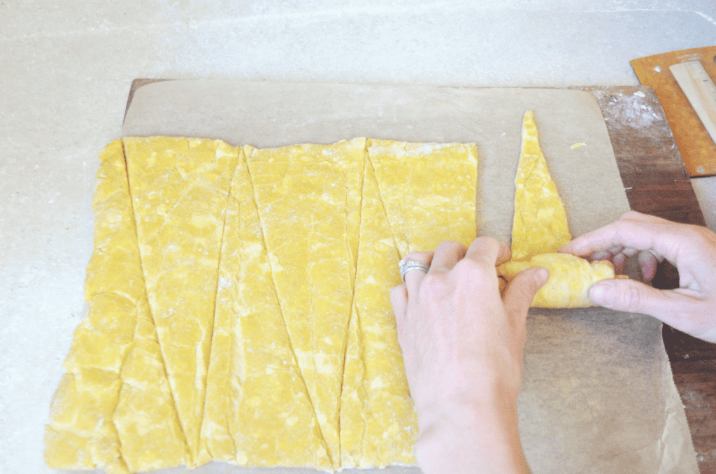 hands roll up a triangle of dough into a croissant.