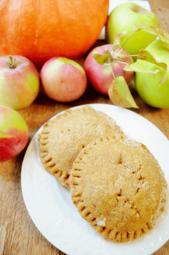 two sugar topped apple hand pies sit among freshly picked apples