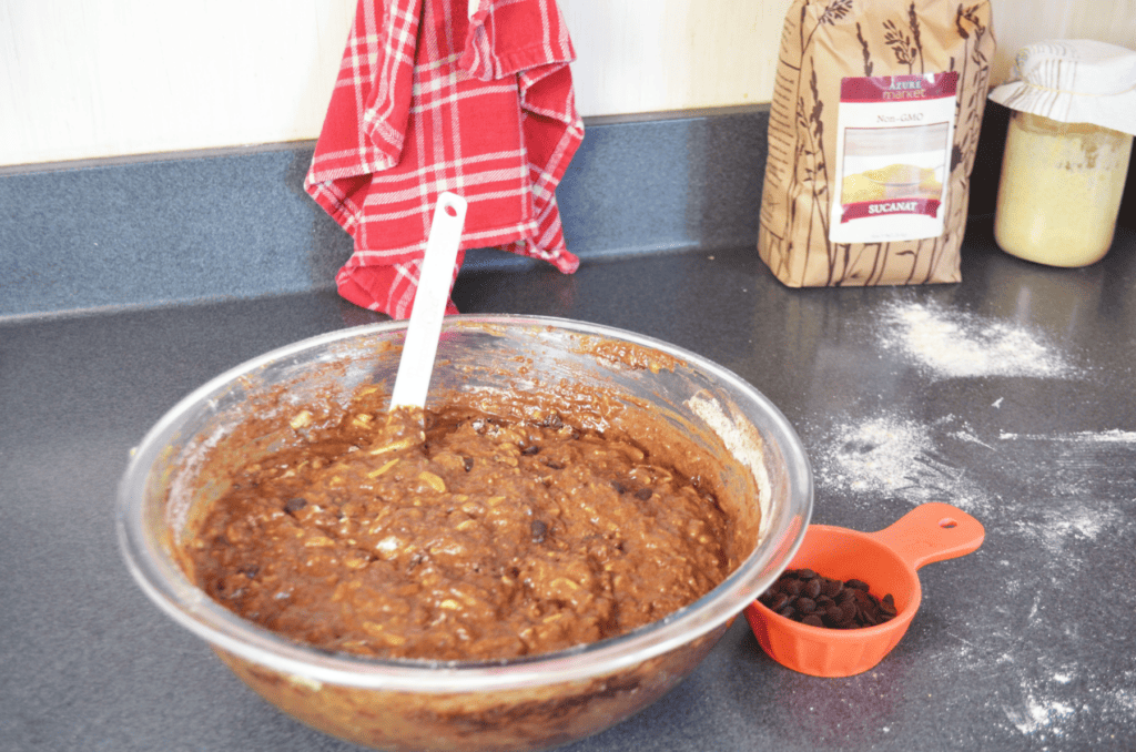 A bowl of zucchini bread batter is blended and ready for the cup of chocolate chips sitting nearby