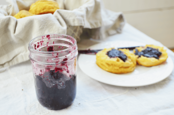 blueberry preserves in a glass jar in front of biscuits