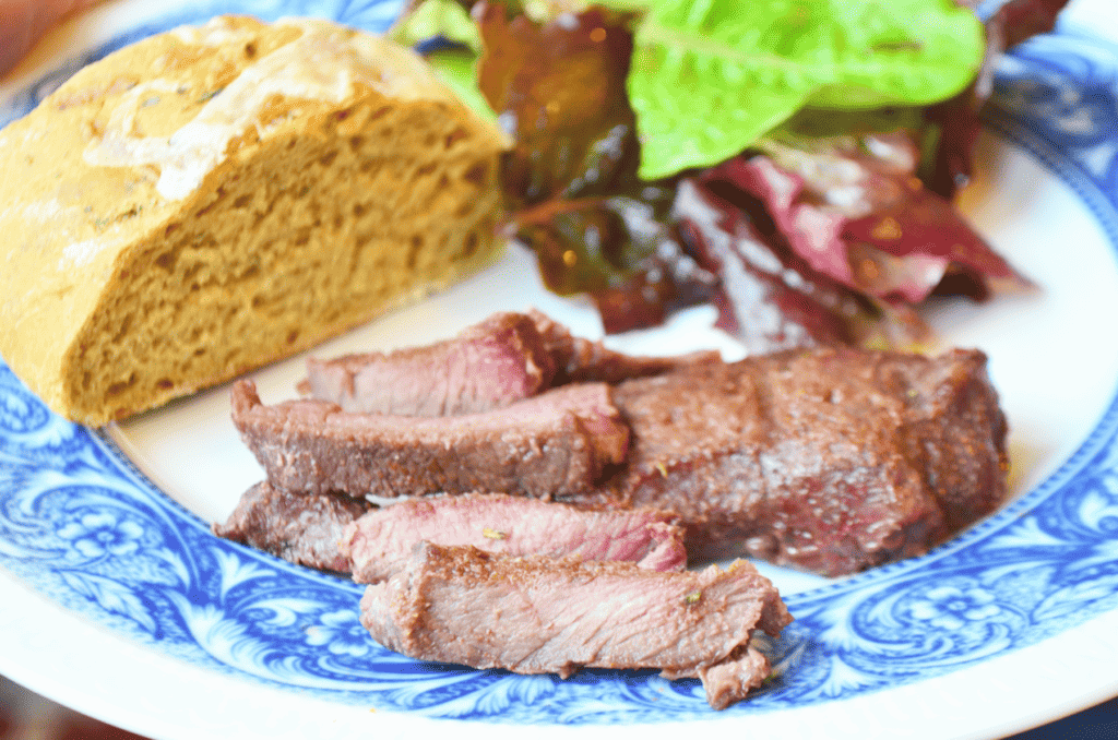 Venison seasoned with savory and sweet dry rub fills a dinner plate with salad and bread