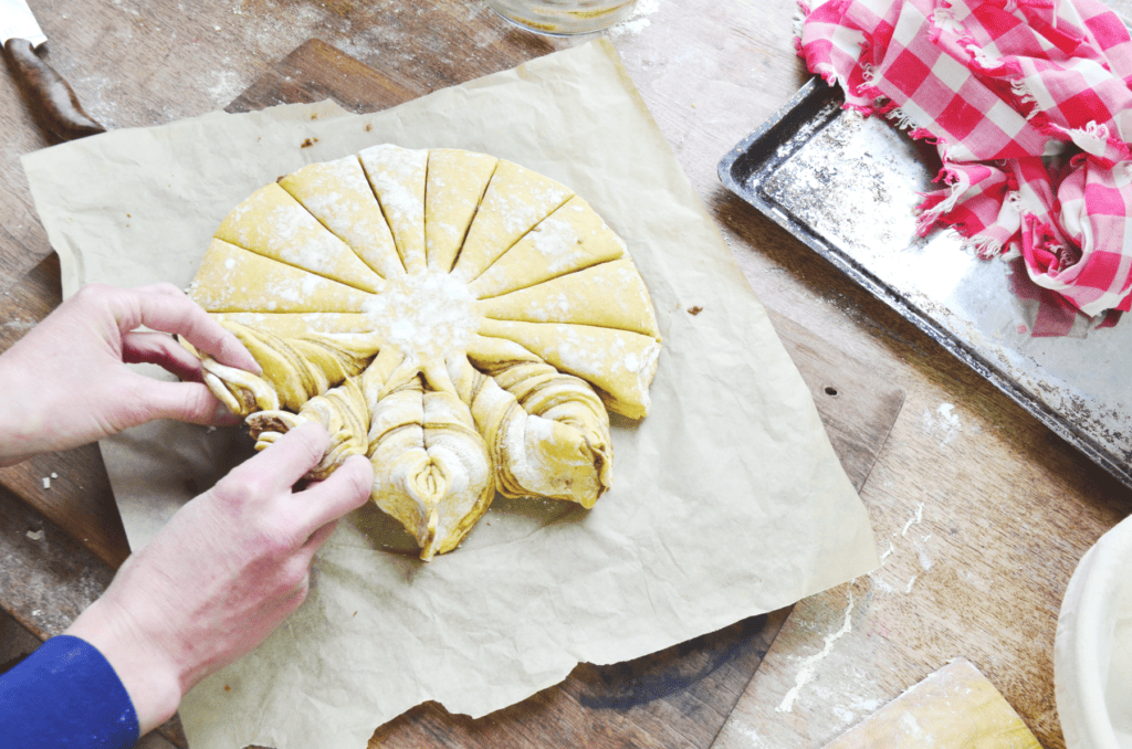 Hands twist sections of dough to shape a snowflake bread