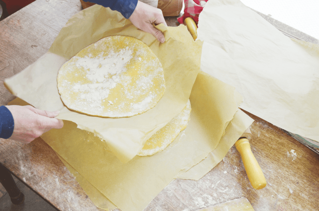Hands stack round rolled dough on parchment paper for a snowflake bread