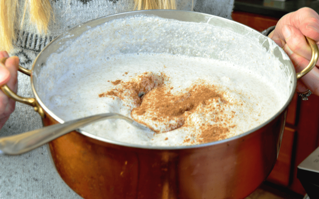 Woman holds a bright copper saucepan filled with soft and light cream of buckwheat cereal. Dark cinnamon is sprinkled of the top.