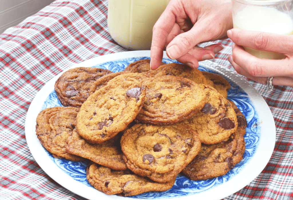 Hand reaches for a whole wheat chocolate chip cookie with einkorn flour  with browned crispy edges and a soft center.