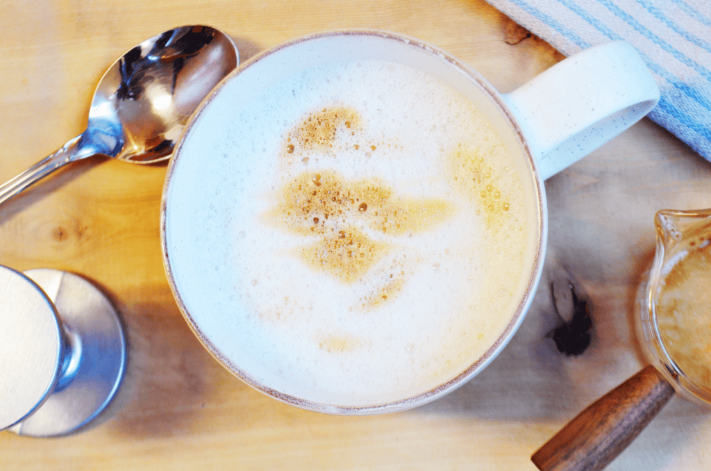 A Cup of foamy milk  and espresso sit on a table with coffee equipment.