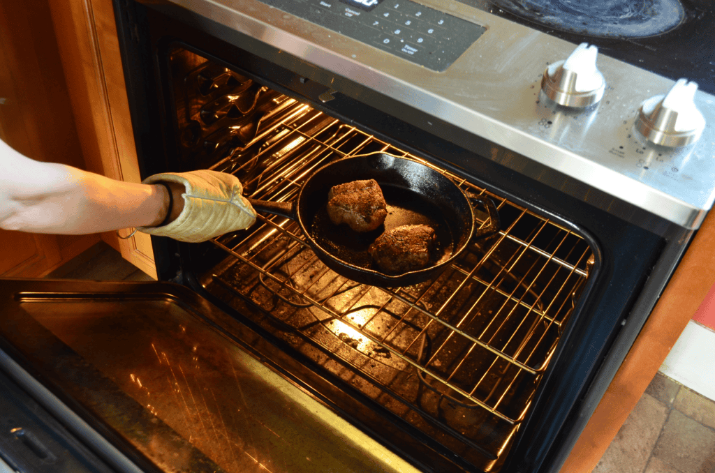 Filet mignon on a cast iron skillet is placed into a hot oven.