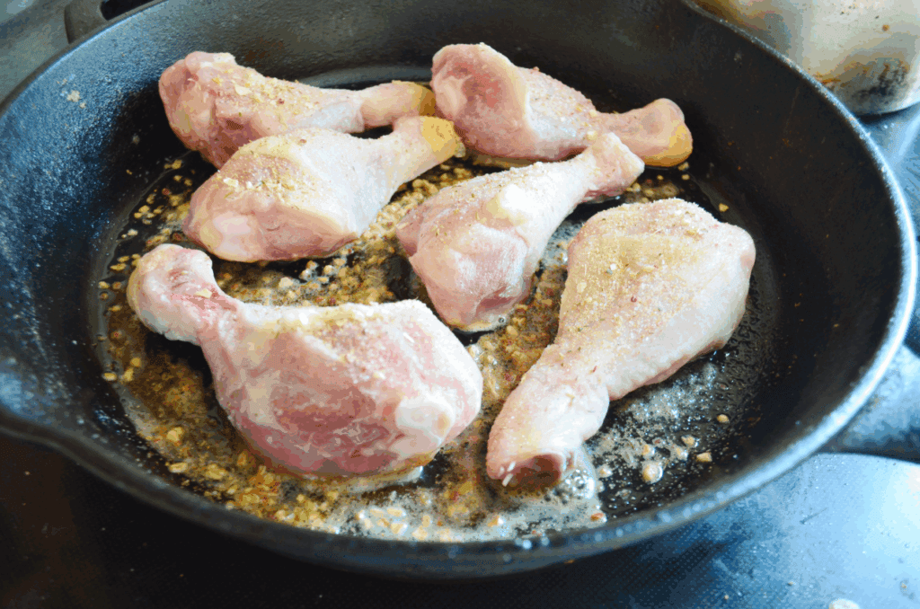 Frozen Chicken Drumsticks sit sprinkled with seasoning in a greased iron skillet ready to be fried