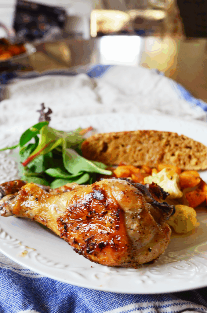 A chicken drumstick made from frozen sits on a dinner plate alongside salad greens, bread and veggies