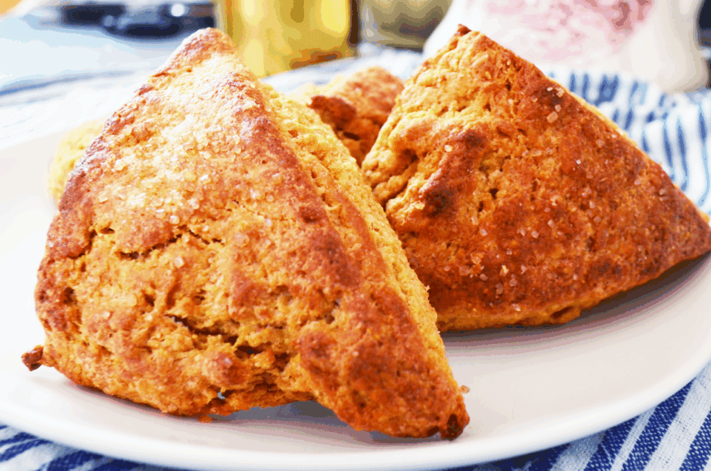 crispy edged scones with sparkling sugar on top sit warm on a plate.