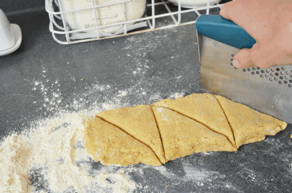 a bench scraper cuts into dough to shape triangular scones before baking.