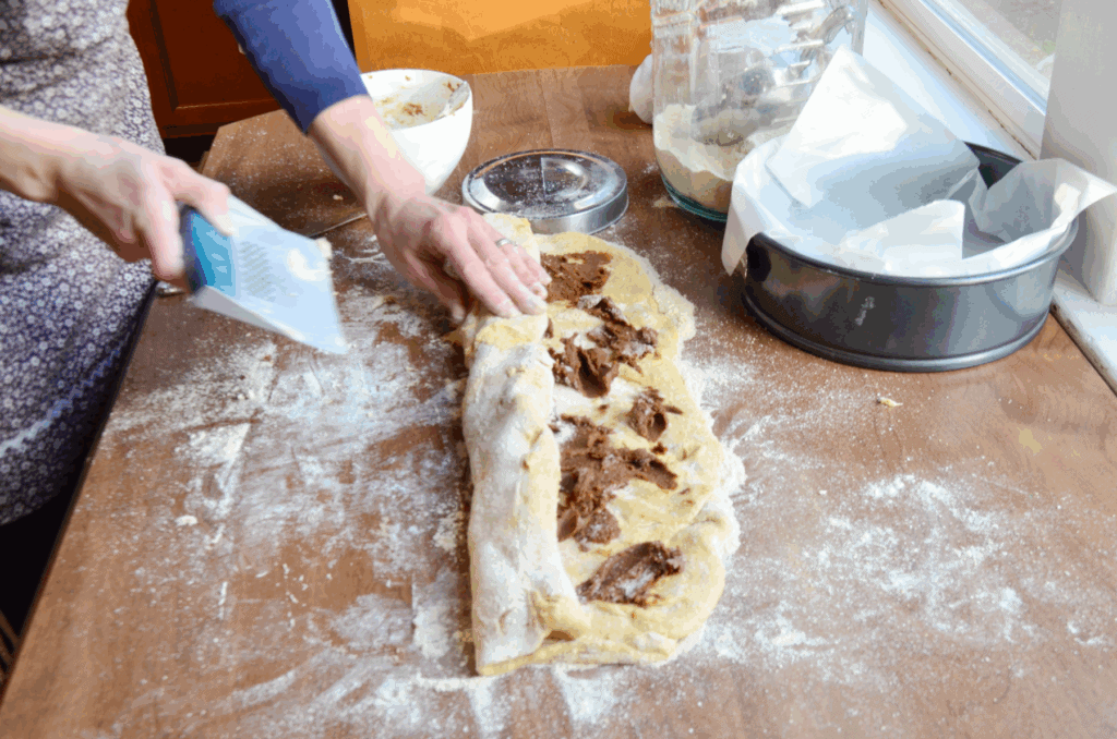 Healthy sourdough dough on a counter being rolled up with a dough scraper.