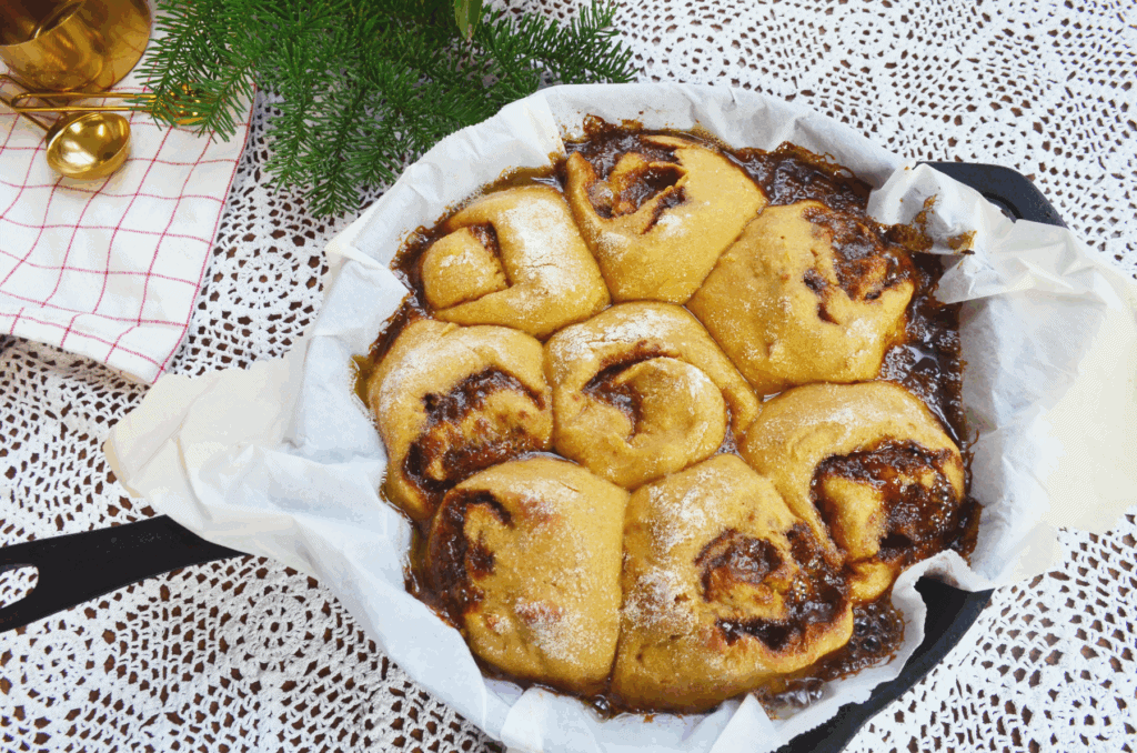 Healthy sourdough cinnamon rolls baked in a cast iron skillet on a table with pretty wintery greenery beside it.