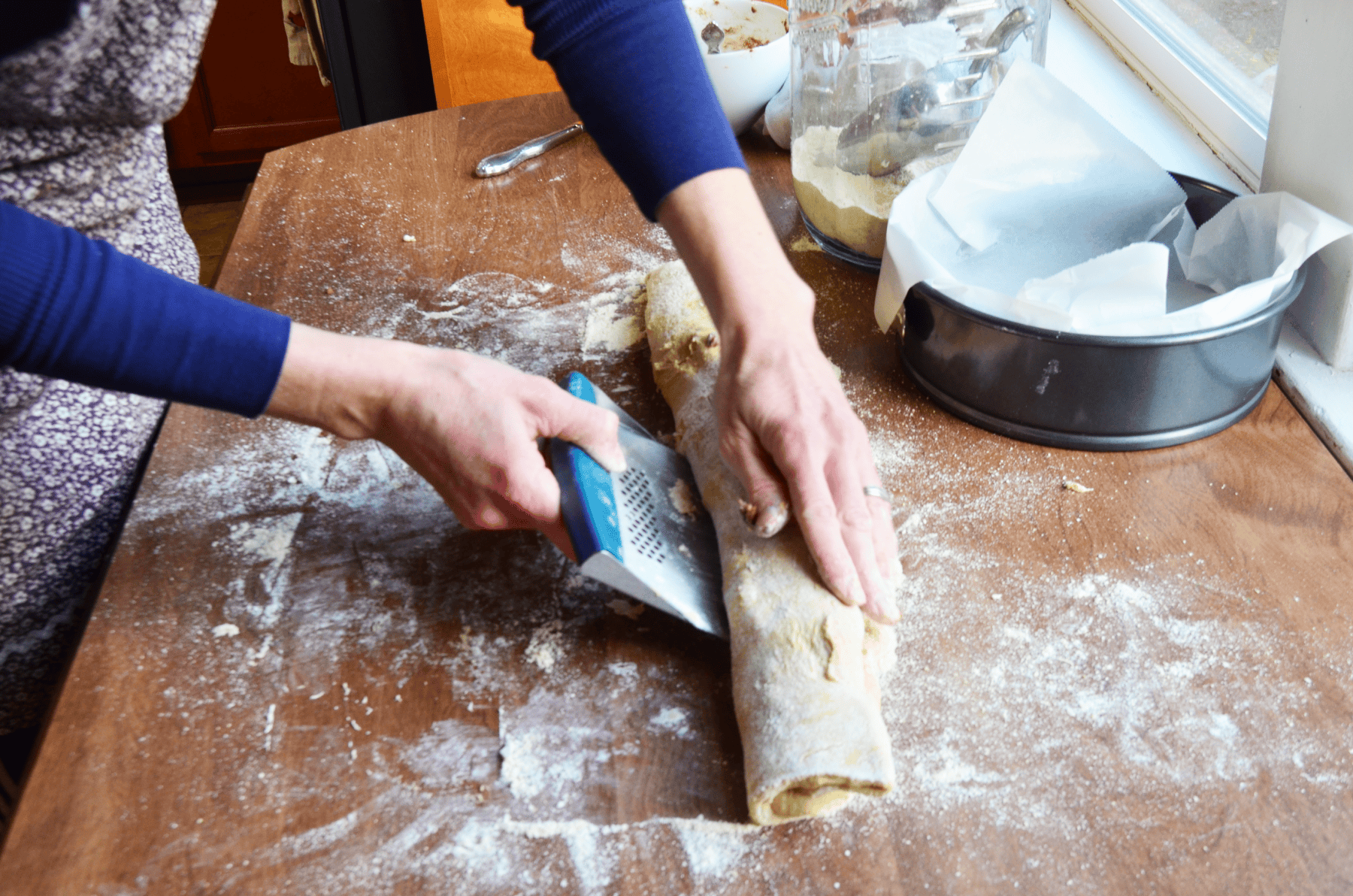 hands roll cinnamon rolls tight on a floured table.