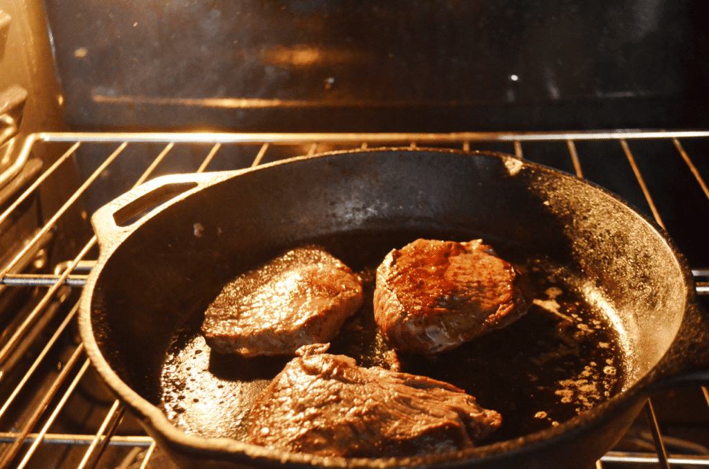 homemade steak being transferred to the oven after searing in a cast iron skillet