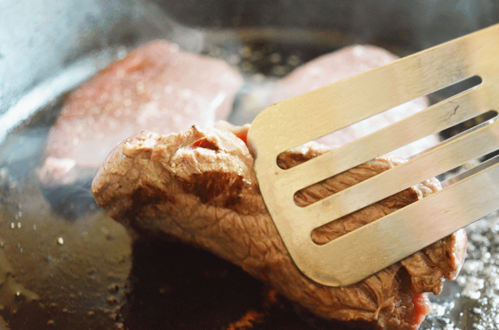 steak being seared in a cast iron skillet being checked with a spatula